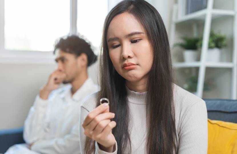 Stressed asian young couple man, woman quarrel on couch, relationship in trouble. Wife hand holding wedding ring in disappointment and upset her husband